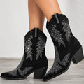 Black suede cowboy boots with silver rhinestone western embroidery, shown on a model's feet against a light gray background.