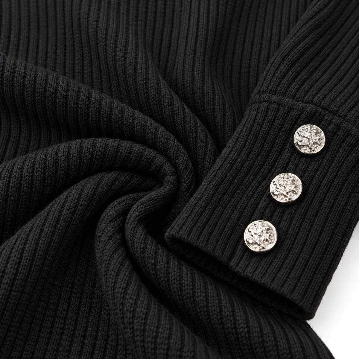 Close-up of a black ribbed knit garment, likely a sweater or jacket sleeve, with three round silver decorative buttons on the cuff against a white background.
