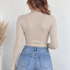 A woman shown from the back wearing a beige ribbed long-sleeve mock neck top and light blue jeans against a white wall.