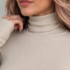 Close-up of a woman wearing a ribbed turtleneck sweater in a light beige color, showing the texture of the knit fabric and her hand resting near her collar.