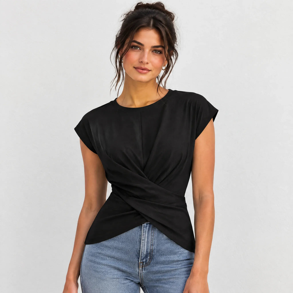 A woman wearing a black short-sleeve top with a twisted wrap-front detail and light blue jeans, photographed against a plain light gray studio background.