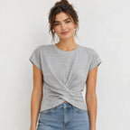 A woman wearing a light gray heathered short-sleeve t-shirt with a twisted knot detail at the front hem, paired with blue jeans, against a plain light gray background.