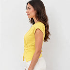 A woman in side profile wearing a bright yellow short-sleeve top with a twisted front detail and white pants, set against a plain white background.