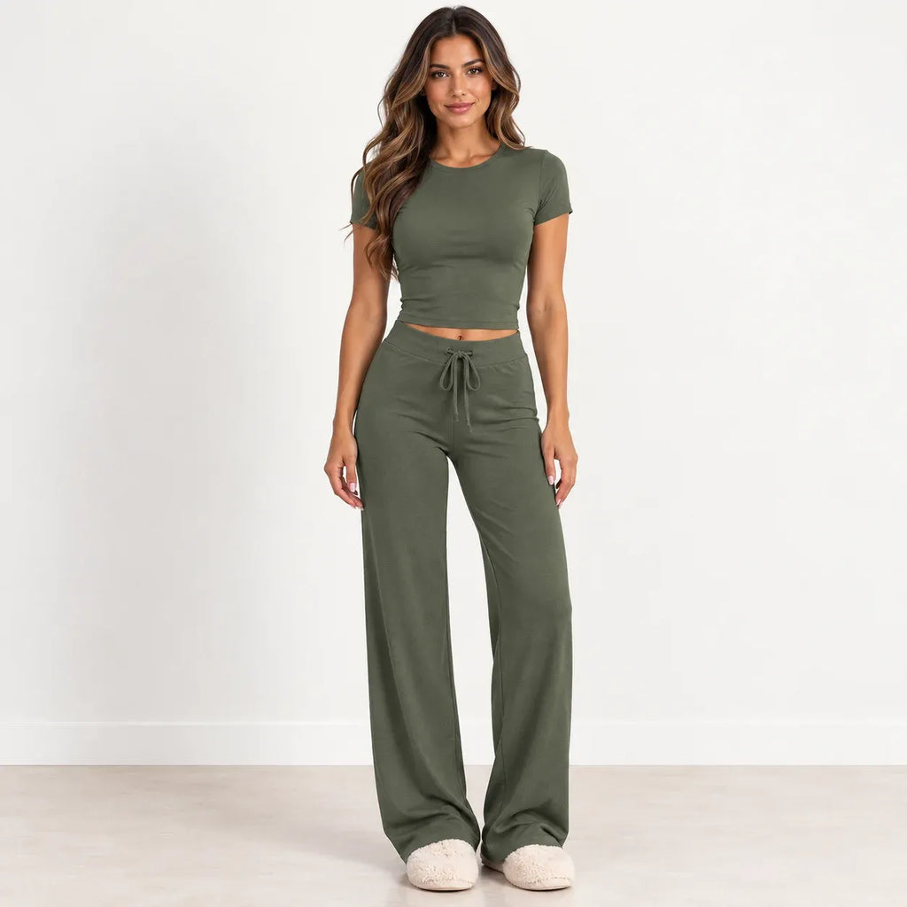 A woman modeling an olive green two-piece lounge set consisting of a short-sleeve crop top and matching wide-leg drawstring pants, standing against a clean white studio background.