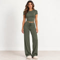 A woman modeling an olive green two-piece lounge set consisting of a short-sleeve crop top and matching wide-leg drawstring pants, standing against a clean white studio background.