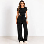 A woman modeling a black short-sleeve crop top and matching black wide-leg drawstring pants against a clean white studio background.