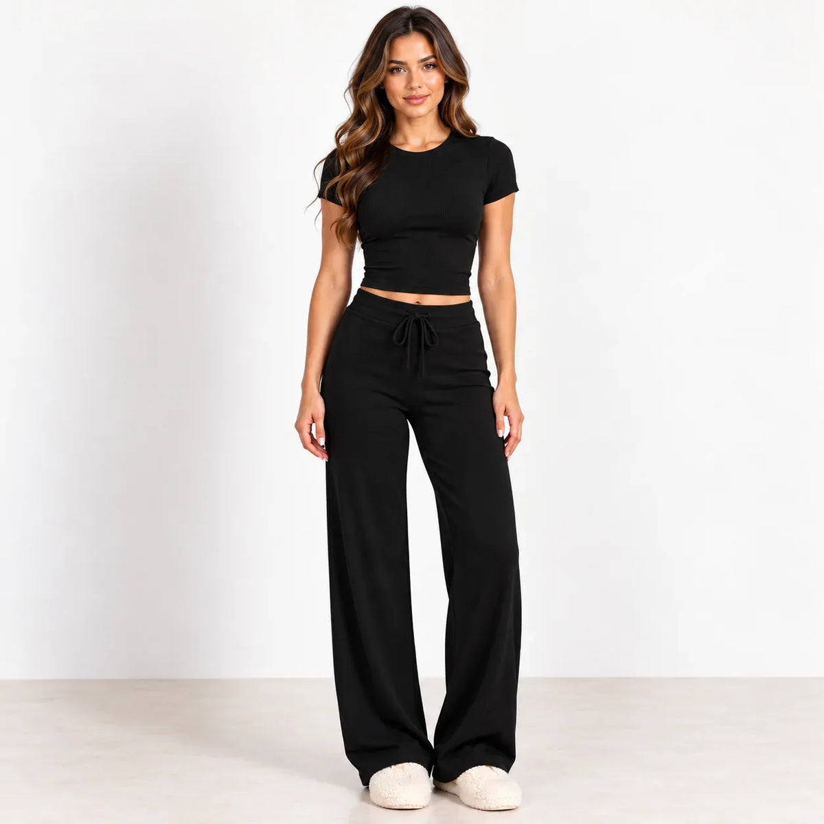 A woman modeling a black short-sleeve crop top and matching black wide-leg drawstring pants against a clean white studio background.