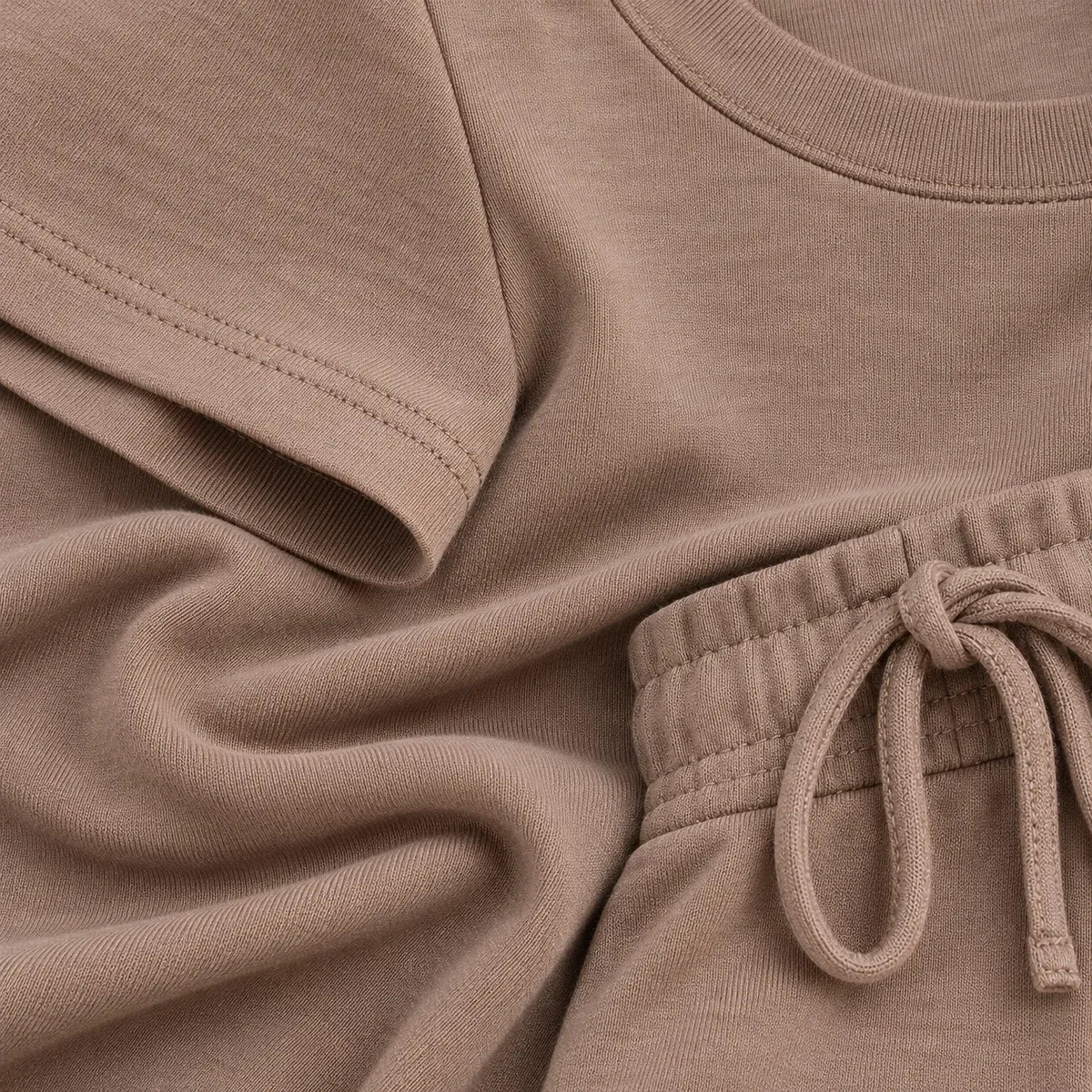 Close-up of a taupe-colored knit loungewear set, showing the texture of a short-sleeve top and matching drawstring shorts.