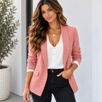 A woman wearing a dusty pink blazer over a white button-up top and black pants, standing in a bright indoor setting with a potted plant in the background.