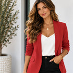 A woman wearing a red blazer over a white top and black pants, standing indoors near a potted plant.
