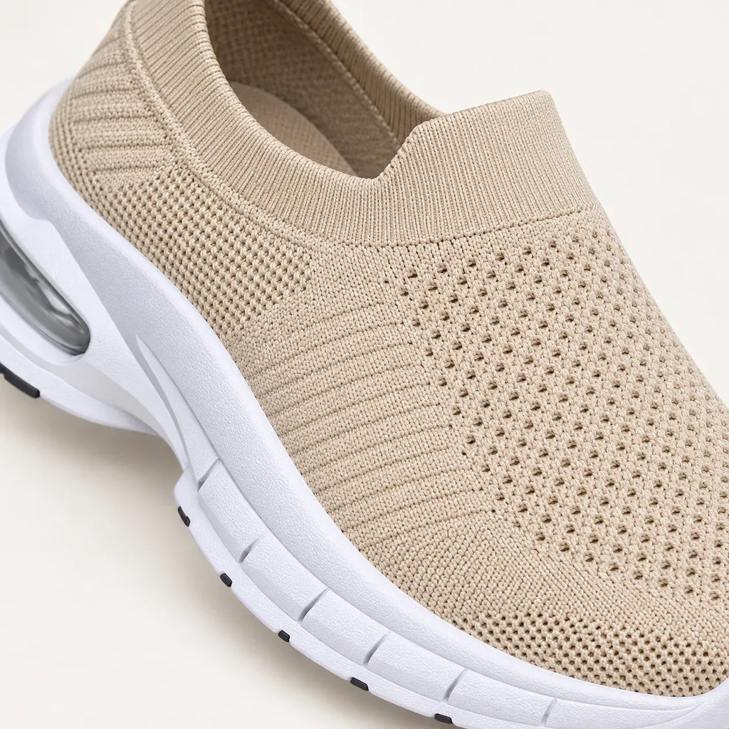 A close up view of beige slip-on knit sneakers with white soles and clear air cushioning.