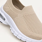 A close up view of beige slip-on knit sneakers with white soles and clear air cushioning.