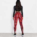 A woman is shown from behind wearing high-waisted red and black snakeskin print leggings, a black long-sleeve crop top, and black and white sneakers against a plain white studio background.