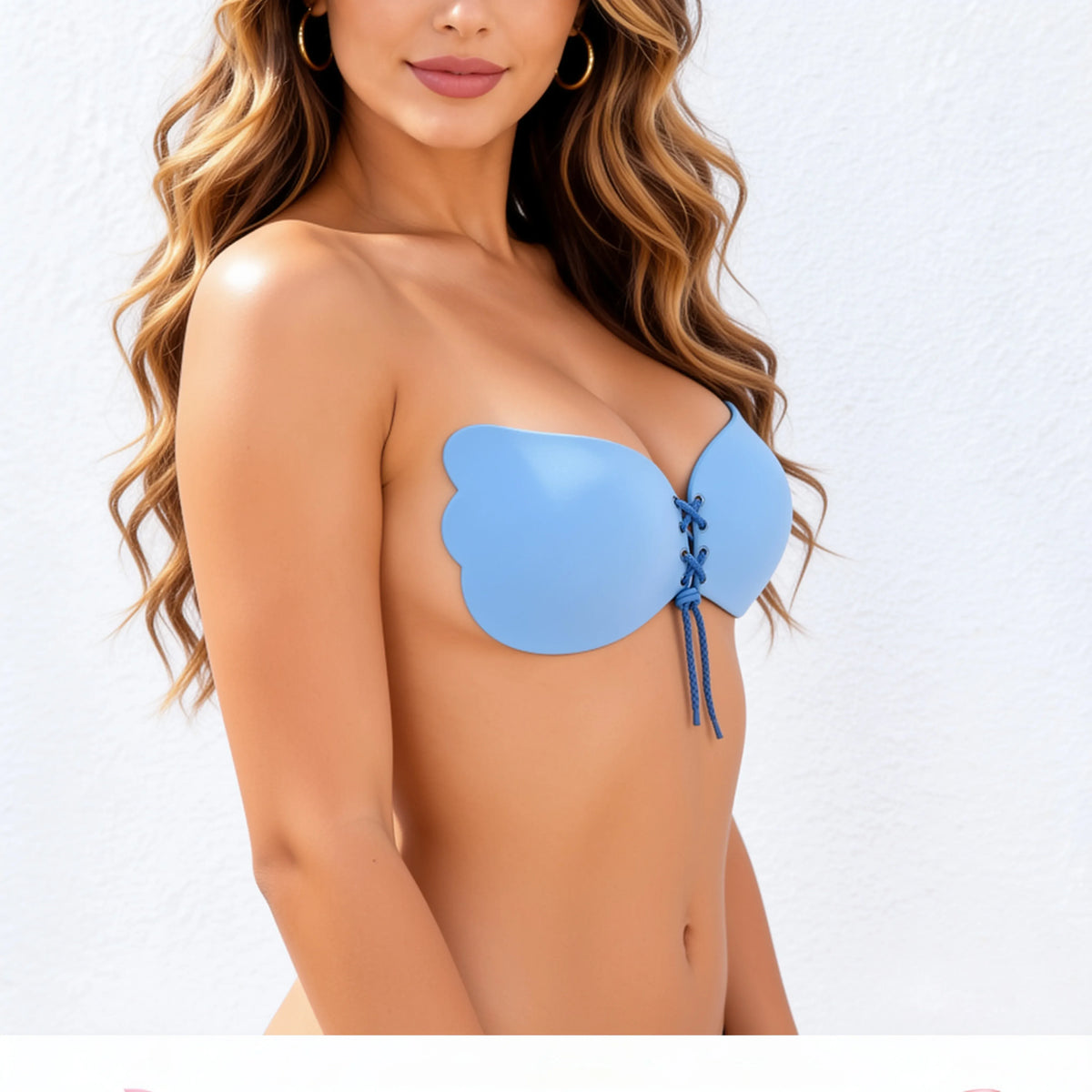 A woman wearing a light blue strapless bandeau-style adhesive bra with lace-up front detail, shown from the shoulders to the hips against a plain white wall.