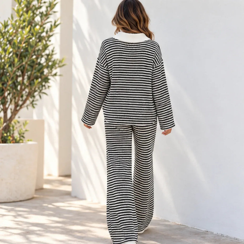 A woman viewed from behind wearing a matching black and white horizontally striped two-piece lounge set, walking outdoors against a white wall.