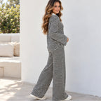 A woman side viewed wearing a matching black and white horizontally striped two-piece lounge set, walking outdoors against a white wall.