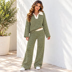 A woman front viewed wearing a matching green and white horizontally striped two-piece lounge set, walking outdoors against a white wall.