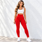 A woman modeling textured red high-waisted leggings and a white sports bra against a white textured wall.