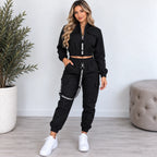 Women’s black utility jogger two-piece set with cropped zip jacket, cargo pockets, elastic jogger cuffs, and black strap details.