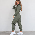 Women’s olive green utility jogger two-piece set shown from the side, featuring a cropped zip jacket, cargo jogger pants, and black strap detail.