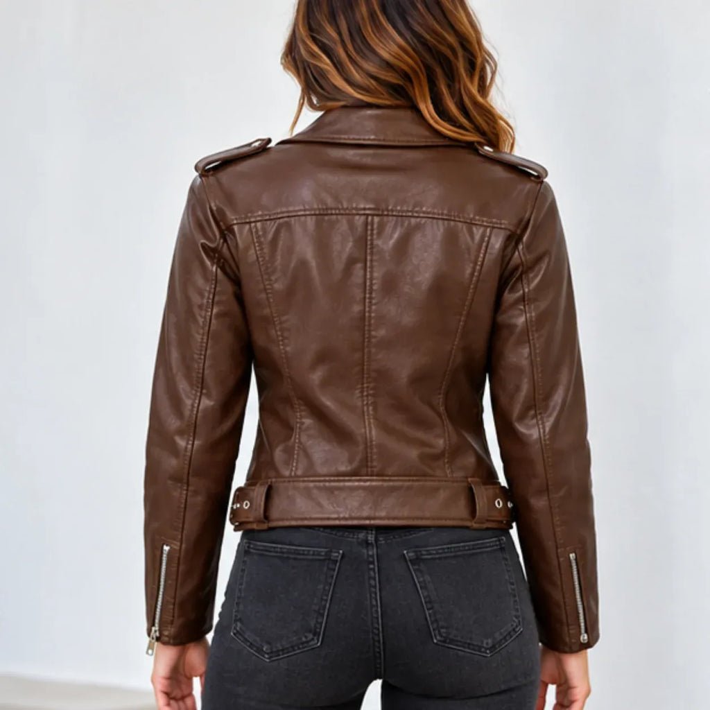 A woman viewed from the back wearing a brown faux-leather moto jacket with silver zipper details and dark gray jeans, set against a plain light gray background.