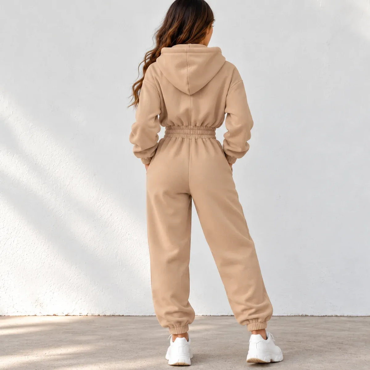 Back view of a beige fleece zip-up hoodie with black drawstrings, black zippers, and silver metal ring hardware.