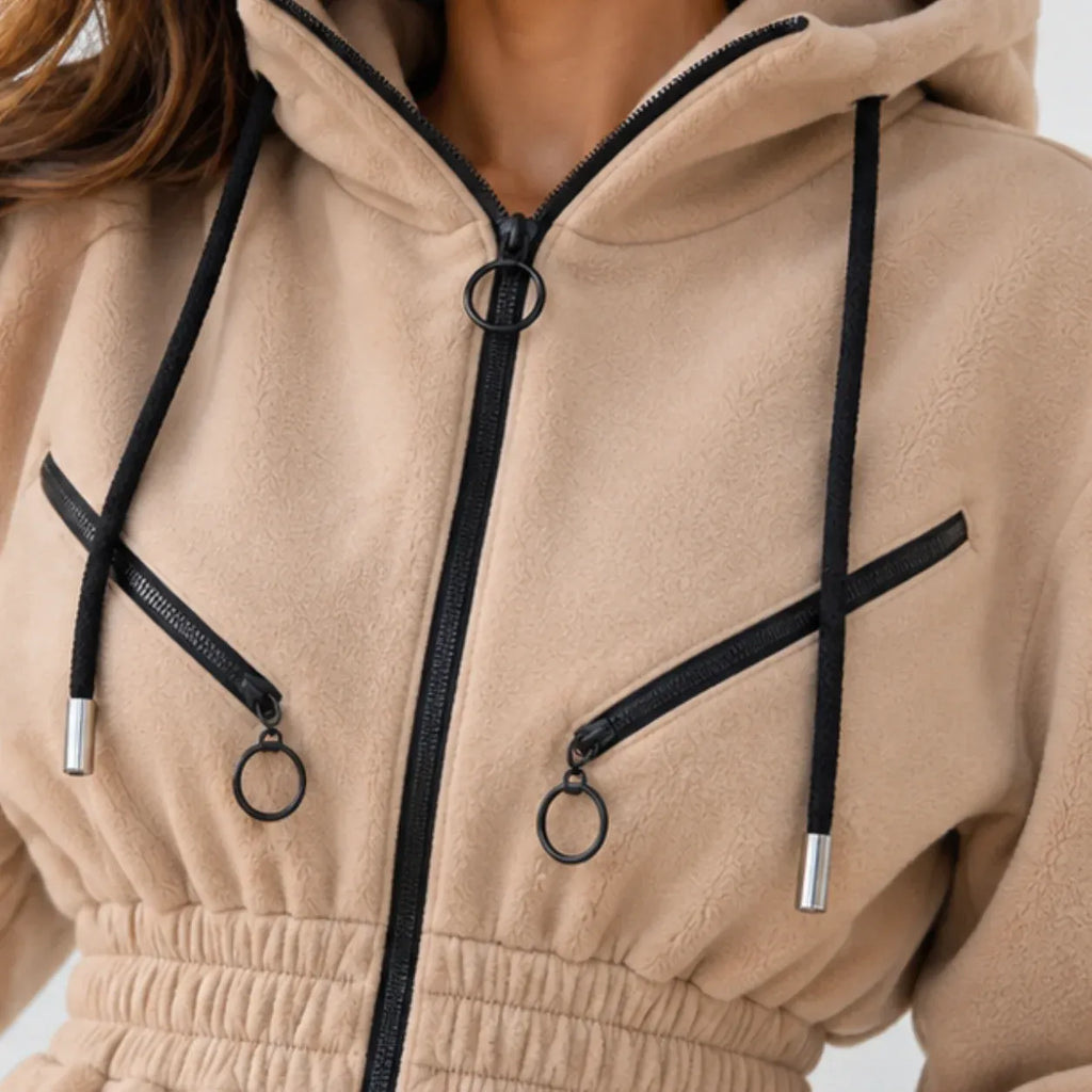 Close-up of a beige fleece zip-up hoodie with black drawstrings, black zippers, and silver metal ring hardware.
