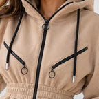Close-up of a beige fleece zip-up hoodie with black drawstrings, black zippers, and silver metal ring hardware.