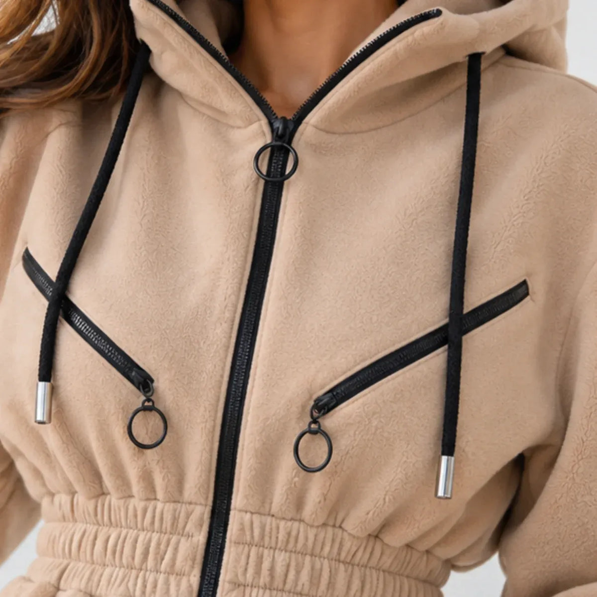 Close-up of a beige fleece zip-up hoodie with black drawstrings, black zippers, and silver metal ring hardware.