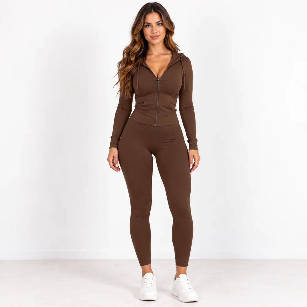A woman modeling a brown zip-up hoodie and matching leggings set, paired with white sneakers, against a plain white studio background.