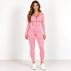 A woman modeling a matching pink long-sleeve zip-up hoodie and high-waisted leggings set, paired with white sneakers, against a plain white studio background.