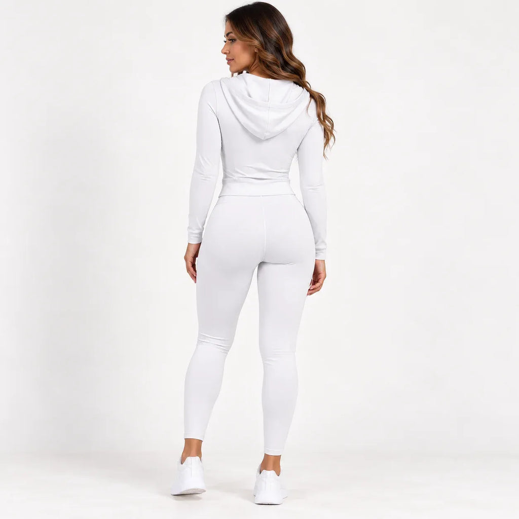 A woman wearing a matching white long-sleeve hooded top and high-waisted leggings, shown from the back against a plain white studio background.