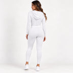 A woman wearing a matching white long-sleeve hooded top and high-waisted leggings, shown from the back against a plain white studio background.