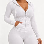 A plus-size model wearing a white long-sleeve zip-up hoodie with a deep V-neckline, side pockets, and matching white leggings, shown against a plain white background.