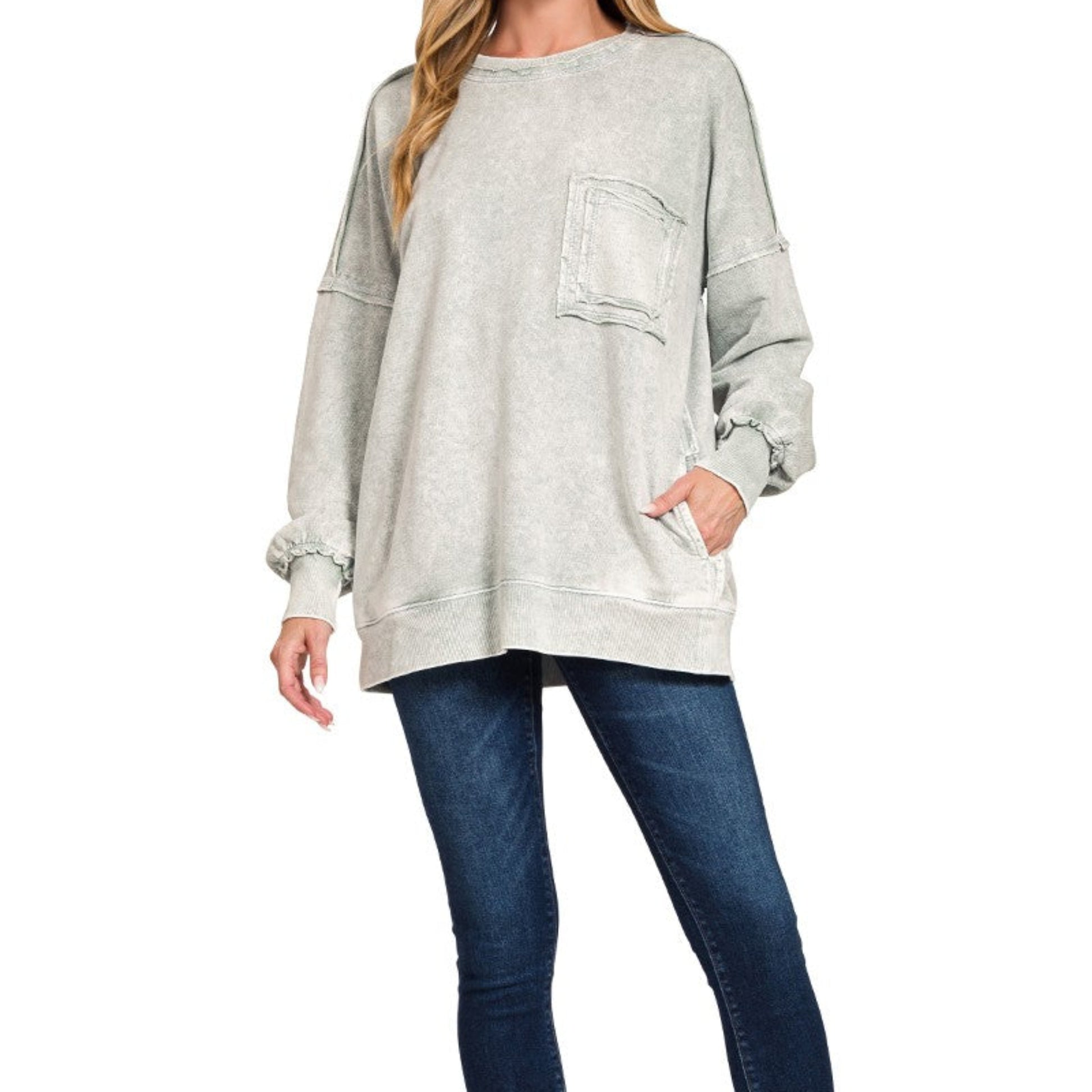 Woman wearing a light gray sweatshirt with a pocket and blue jeans on a white background