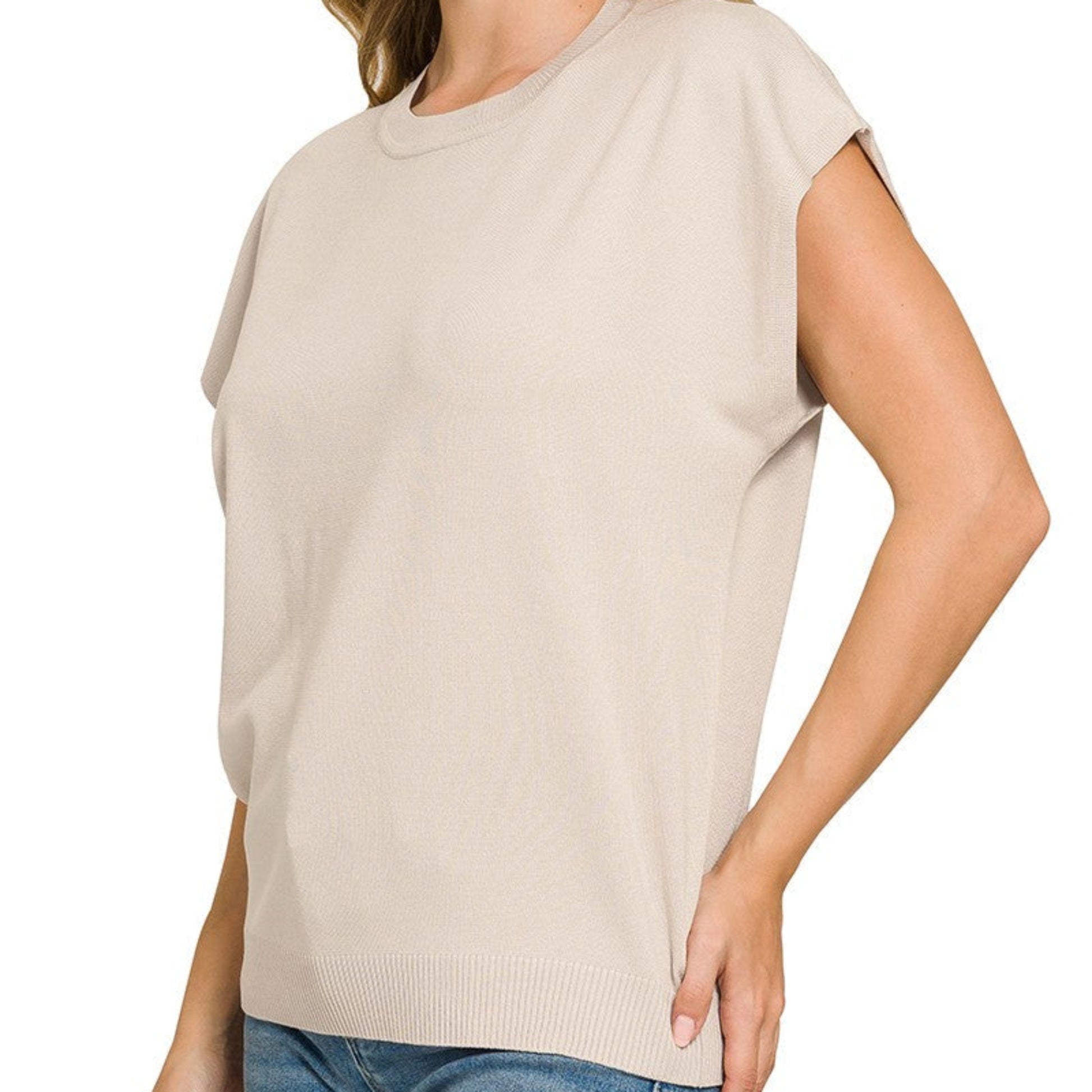 Woman wearing a beige sleeveless top and blue jeans on a white background