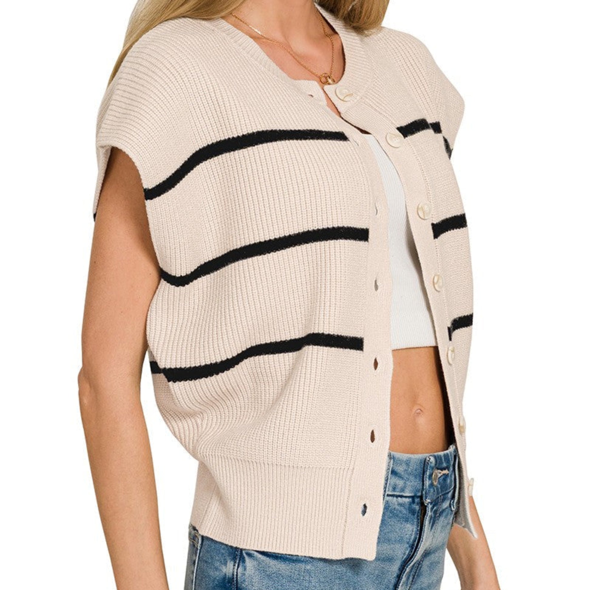 Woman wearing a sand beige cardigan with black stripes and blue jeans on a white background
