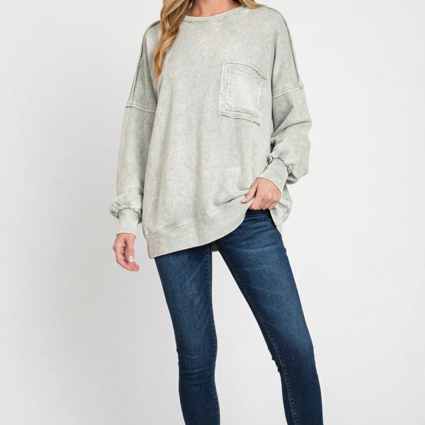 Woman wearing a light gray oversized sweater and blue jeans on a white background