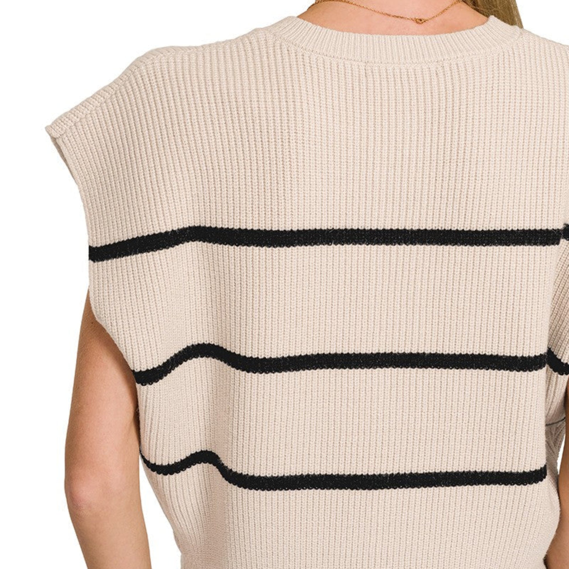 Beige sleeveless top with black stripes worn by a person on a white background