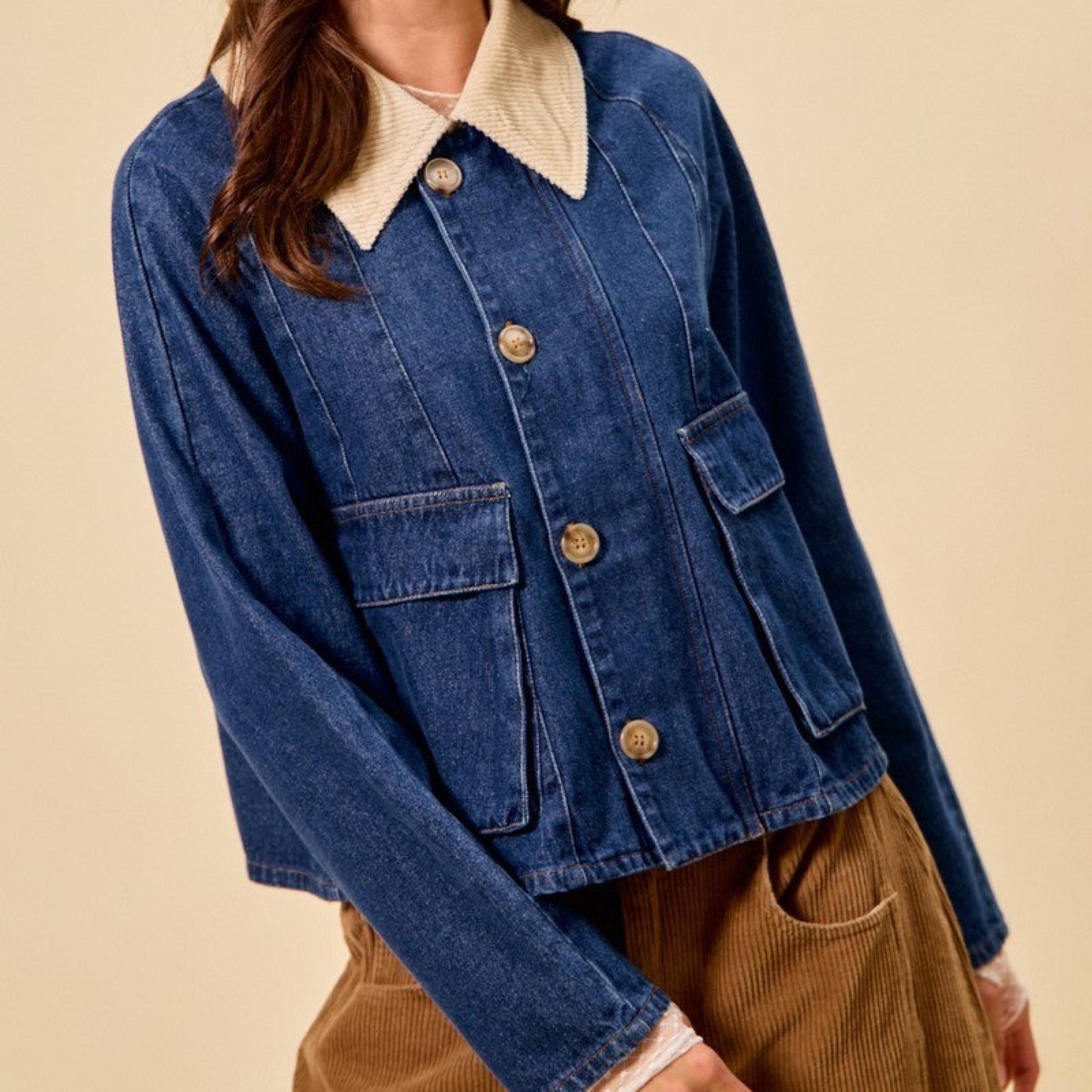 Woman wearing a blue denim jacket with a cream collar and beige pants against a beige background