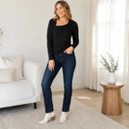 Women's black asymmetrical long sleeve top with a modern asymmetrical neckline, front view paired with dark wash jeans in a neutral lifestyle setting.