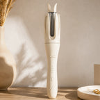 Ivory automatic rotating curling iron standing on a vanity with modern home décor.