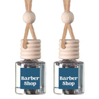 Two small clear glass reed diffusers with beige wooden tops and hanging cords, each labeled Barber Shop, on a white background.