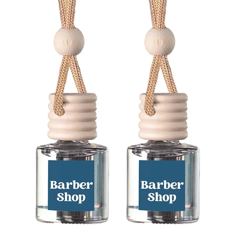 Two small clear glass reed diffusers with beige wooden tops and hanging cords, each labeled Barber Shop, on a white background.