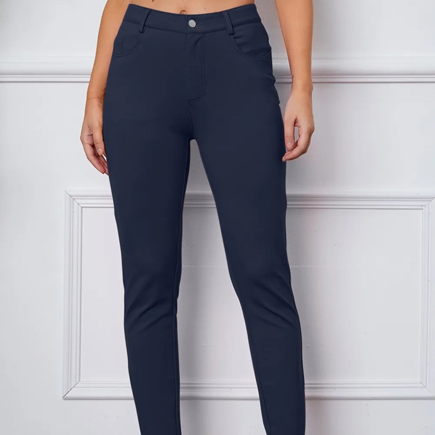 Navy blue pants worn by a person against a white paneled wall.