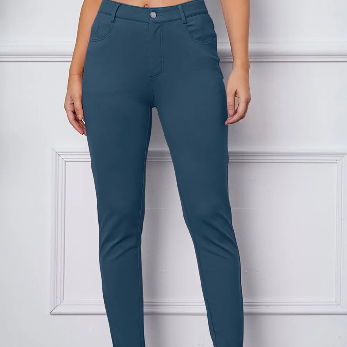 Teal pants worn by a person against a white paneled wall