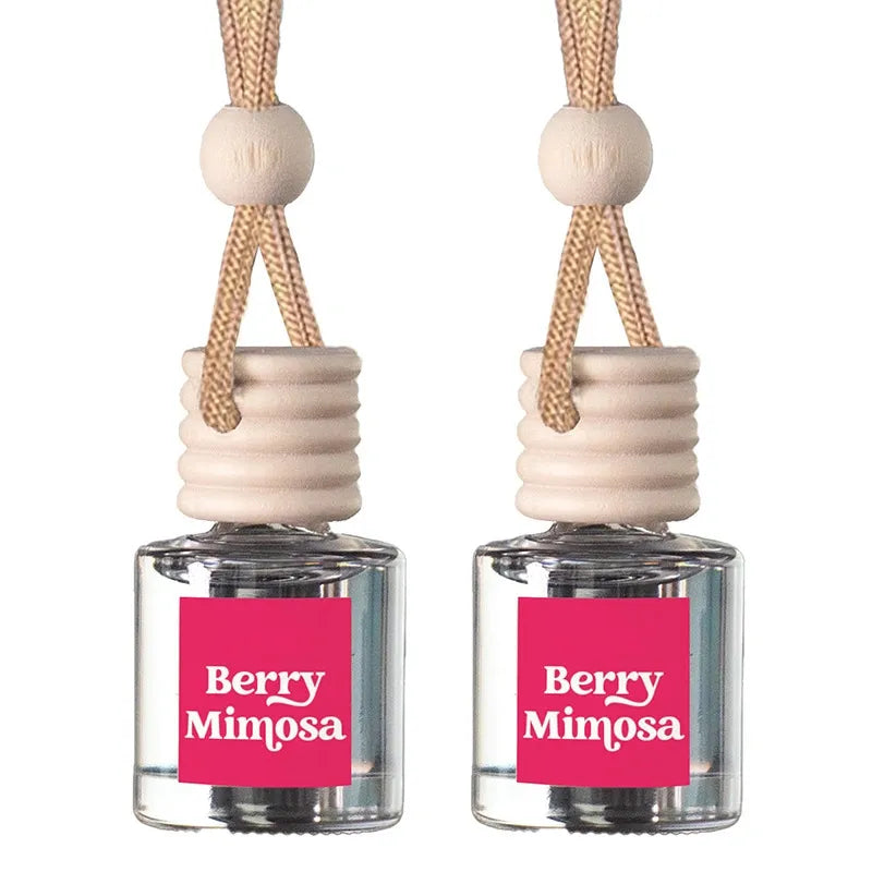 Two Berry Mimosa reed diffusers with clear glass bottles, pink labels, beige wooden stoppers, and natural fiber hanging cords on a white background.