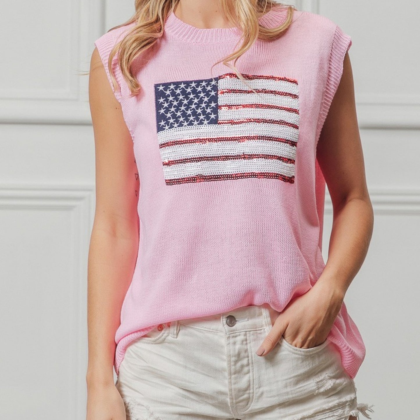 Person wearing a pink sleeveless sweater with an American flag design against a white background