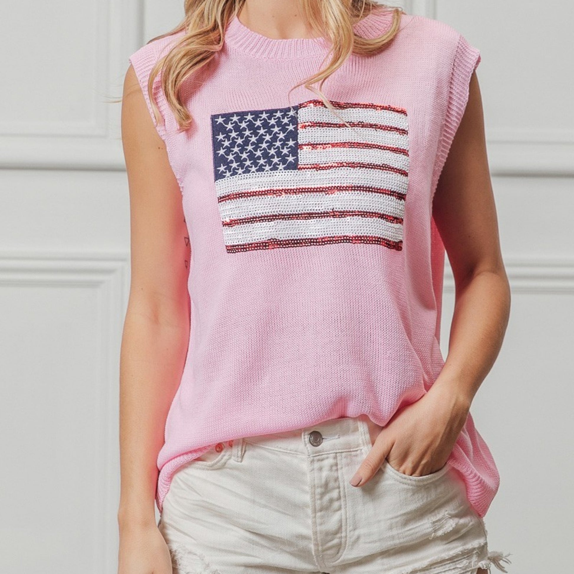 Person wearing a pink sleeveless sweater with an American flag design against a white background
