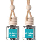 Two clear glass reed diffuser bottles with beige wooden caps, hanging cords, and turquoise labels reading 'Birthday Cake' on a white background.